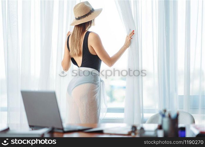 Female person in swimsuit looks at the window in office, dreaming about a vacation concept. Daydreaming about a journey idea