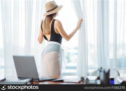 Female person in swimsuit looks at the window in office, dreaming about a vacation concept. Daydreaming about a journey idea