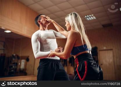 Female person makes pain in the eyes, self-defense workout with male personal trainer, gym interior on background. Woman on self defense training