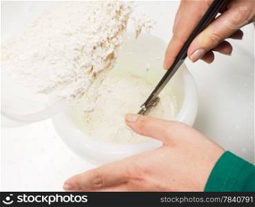 Female person mixing flour into the melted blend of butter and egg yolk with a black spatula