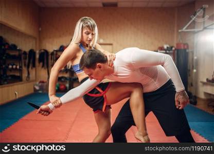 Female person practicing a knee kick to the stomach on self defense workout with male personal trainer, gym interior on background. Woman on training, self-defense practice. Female person practicing knee kick to the stomach