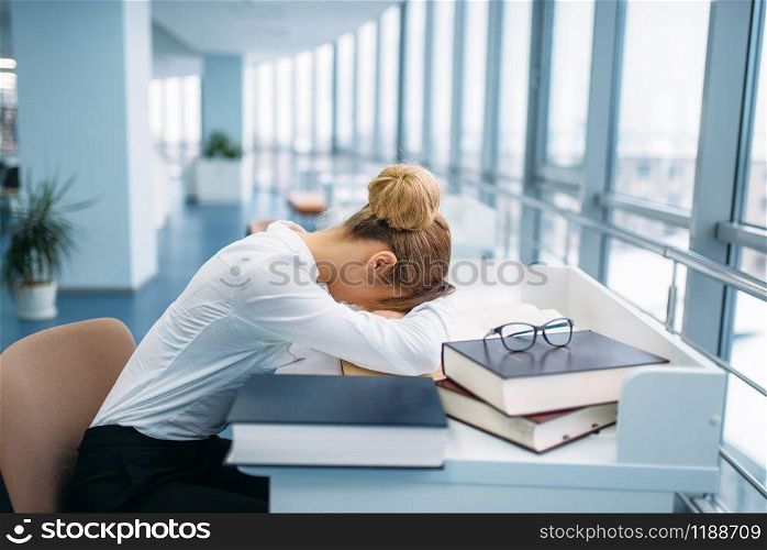 Female person sleeping at the table in library. Young woman in reading room, knowledge depository. Female person sleeping at the table in library
