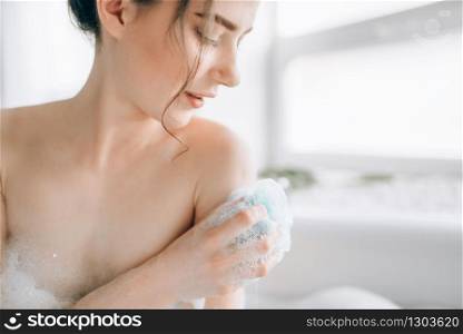Female person soaps the body with a sponge in bath closeup. Bodycare and skincare in bathroom. Female person soaps the body with a sponge