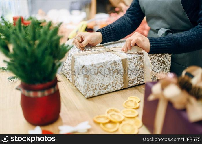 Female person ties a gold bow on gift box, handmade wrapping and decoration process. Woman wraps present on the table, decor procedure. Female person ties a gold bow on gift box