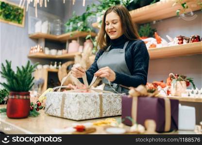 Female person ties a gold bow on gift box, handmade wrapping and decoration process. Woman wraps present on the table, decor process. Female person ties a gold bow on gift box