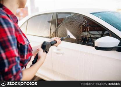 Female person wash off the foam from the car glass. Woman on self-service automobile washing. Outdoor vehicle cleaning at summer day. Female person wash off the foam from the car glass