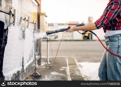 Female person with high pressure water gun in hands cleans car mats, touchless carwash. Young woman on self-service automobile washing. Outdoor vehicle cleaning at summer day