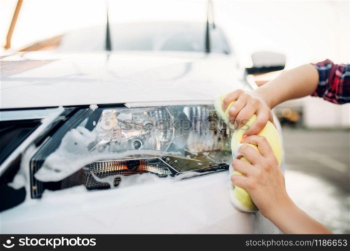 Female person with sponge cleans vehicle headlight, car wash. Young woman on self-service automobile washing. Outdoor carwash at summer day