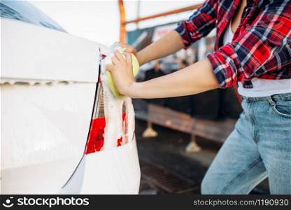 Female person with sponge scrubbing vehicle rear lights with foam, car wash. Young woman on self-service automobile washing. Outdoor carwash at summer day