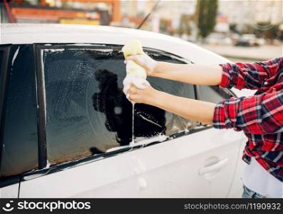 Female person with sponge scrubbing vehicle window with foam, car wash. Young woman on self-service automobile washing. Outdoor carwash at summer day