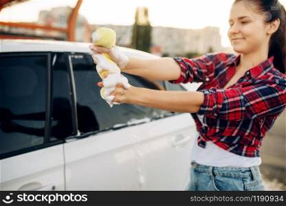 Female person with sponge scrubbing vehicle window with foam, car wash. Young woman on self-service automobile washing. Outdoor carwash. Female person scrubbing vehicle window with foam