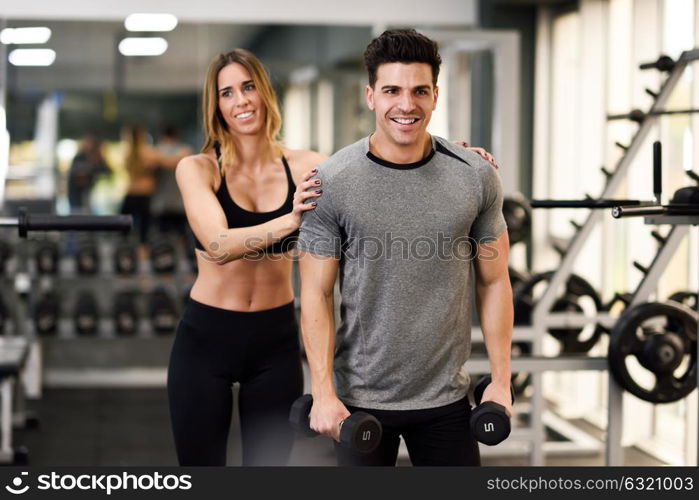 Female personal trainer helping a young man lift dumbells while working out in a gym