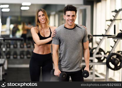 Female personal trainer helping a young man lift dumbells while working out in a gym