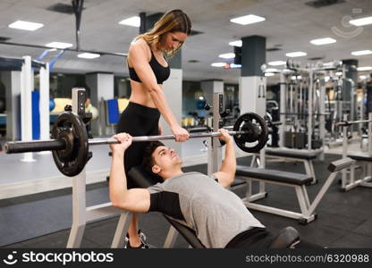 Female personal trainer helping a young man lift weights while working out in a gym