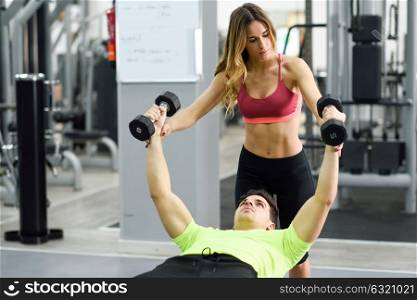 Female personal trainer helping a young man lift weights while working out in a gym