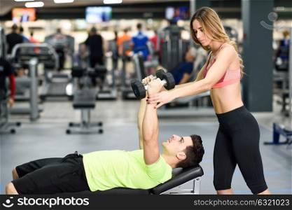 Female personal trainer helping a young man lift weights while working out in a gym