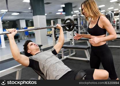 Female personal trainer motivating a young man lift weights while working out in a gym