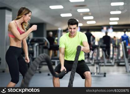 Female personal trainer motivating young man with battle ropes exercise in the fitness gym.