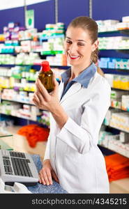 Female pharmacist is standing in her drugstore behind the counter and holds a medicine bottle