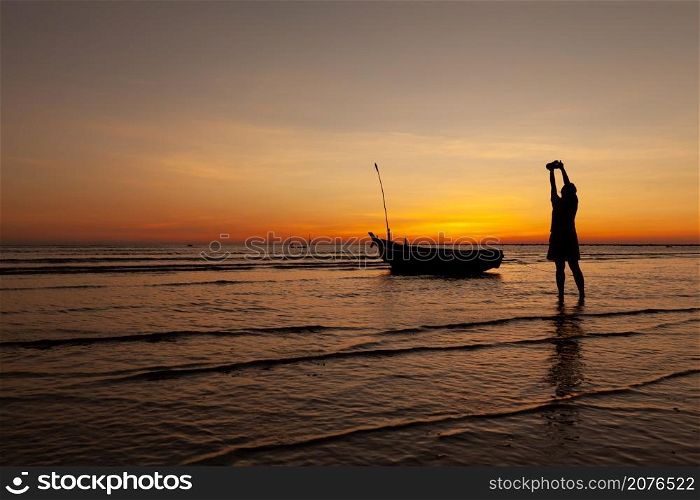Female photographer raised the camera to take a picture in twilight time at the beach in phangnga, Thailand