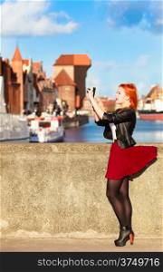 Female photographer taking pictures. Traveler woman red haired fashion girl with camera outdoors in european city, old town Gdansk river Motlawa in the background, Poland Europe