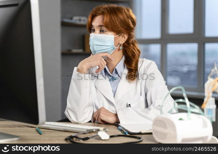 female physician her desk with medical mask looking computer