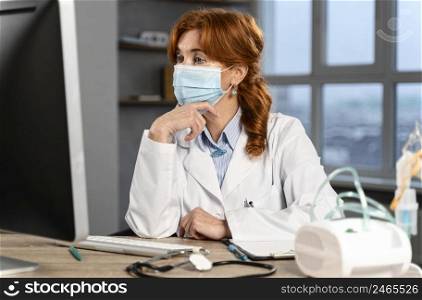 female physician her desk with medical mask looking computer