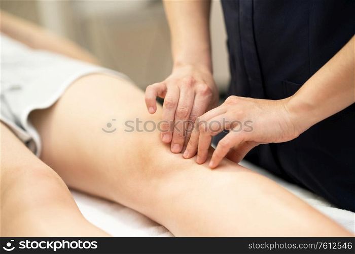 Female Physiotherapist woman doing a treatment on a young woman&rsquo;s knee.. Physiotherapist woman doing a treatment on a woman&rsquo;s knee.