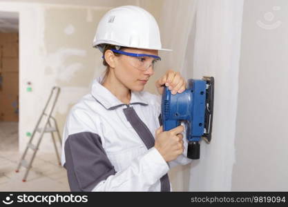 female plasterer sanding the wall using a power sander