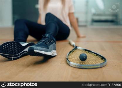 Female player with squash racket and ball sits on the floor. Girl on game training, active sport hobby on court. Player with squash racket and ball sits on floor