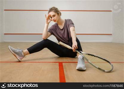 Female player with squash racket sitting on the floor. Girl on game training, active sport hobby on court. Female player with squash racket sitting on floor
