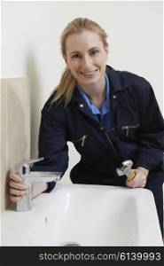 Female Plumber Working On Sink Using Wrench