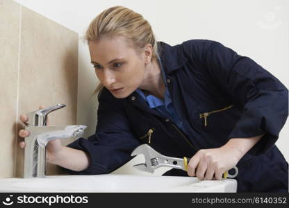 Female Plumber Working On Sink Using Wrench