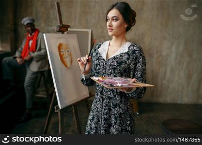 Female portrait painter and male model in art studio. Artist standing at her workplace, cute creative master in workshop, paintbrush creativity. Female portrait painter and male model in studio