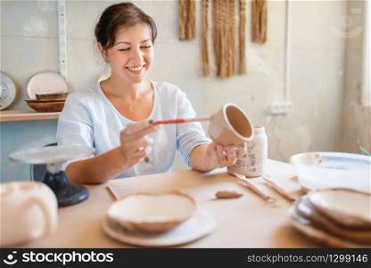 Female potter paints a pot, pottery workshop. Woman molding a bowl. Handmade ceramic art, tableware from clay. Female potter paints a pot, pottery workshop