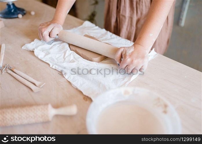 Female potter roll out the foarm with a rolling pin, pottery workshop. Woman molding working material. Handmade ceramic art, tableware from clay. Female potter roll out foarm with a rolling pin