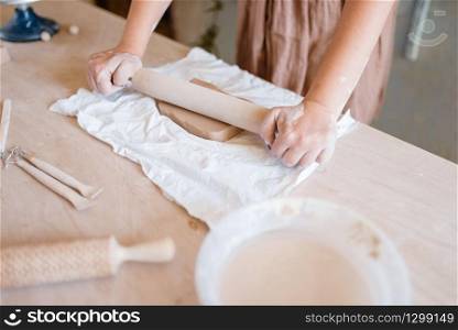 Female potter roll out the foarm with a rolling pin, pottery workshop. Woman molding working material. Handmade ceramic art, tableware from clay. Female potter roll out foarm with a rolling pin