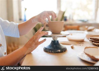 Female potter skins pot with her fingers, pottery workshop. Woman molding a bowl. Handmade ceramic art, tableware from clay. Female potter skins pot with her fingers