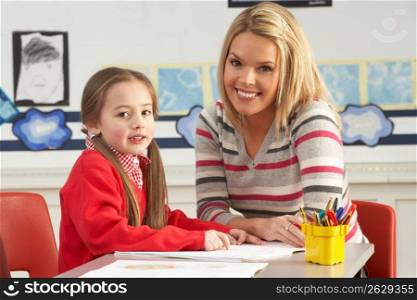 Female Primary School Pupil And Teacher Working At Desk In Classroom