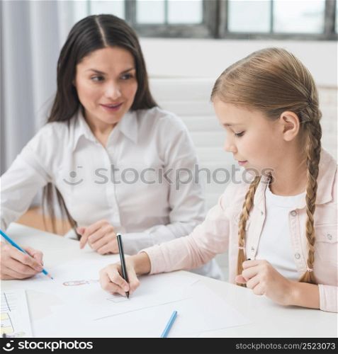 female psychologist looking girl drawing with colored pencil