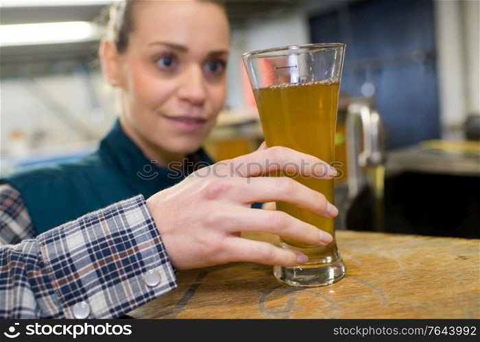 female quality control worker in brewery inspecting glass of ale