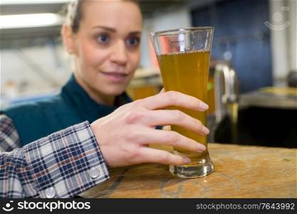 female quality control worker in brewery inspecting glass of ale