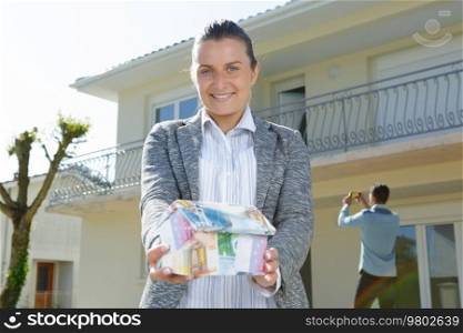 female real estate agent holding house model made of money