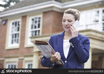 Female Realtor On Phone Outside Residential Property