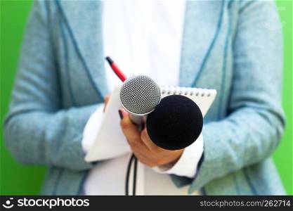 Female reporter at press conference, writing notes, holding microphone