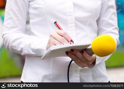 Female reporter at press conference, writing notes, holding microphone