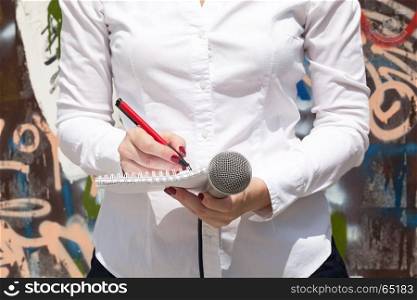 Female reporter at press event, taking notes, holding microphone