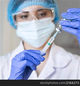 female researcher with safety glasses medical mask holding syringe
