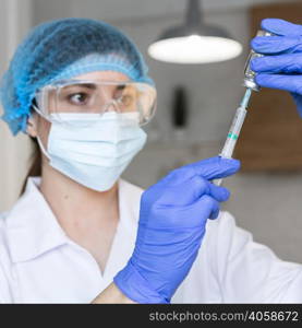 female researcher with safety glasses medical mask holding syringe vaccine
