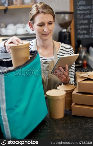 Female Restaurant Worker With Digital Tablet Packing Insulated Bag For Takeaway Food Home Delivery